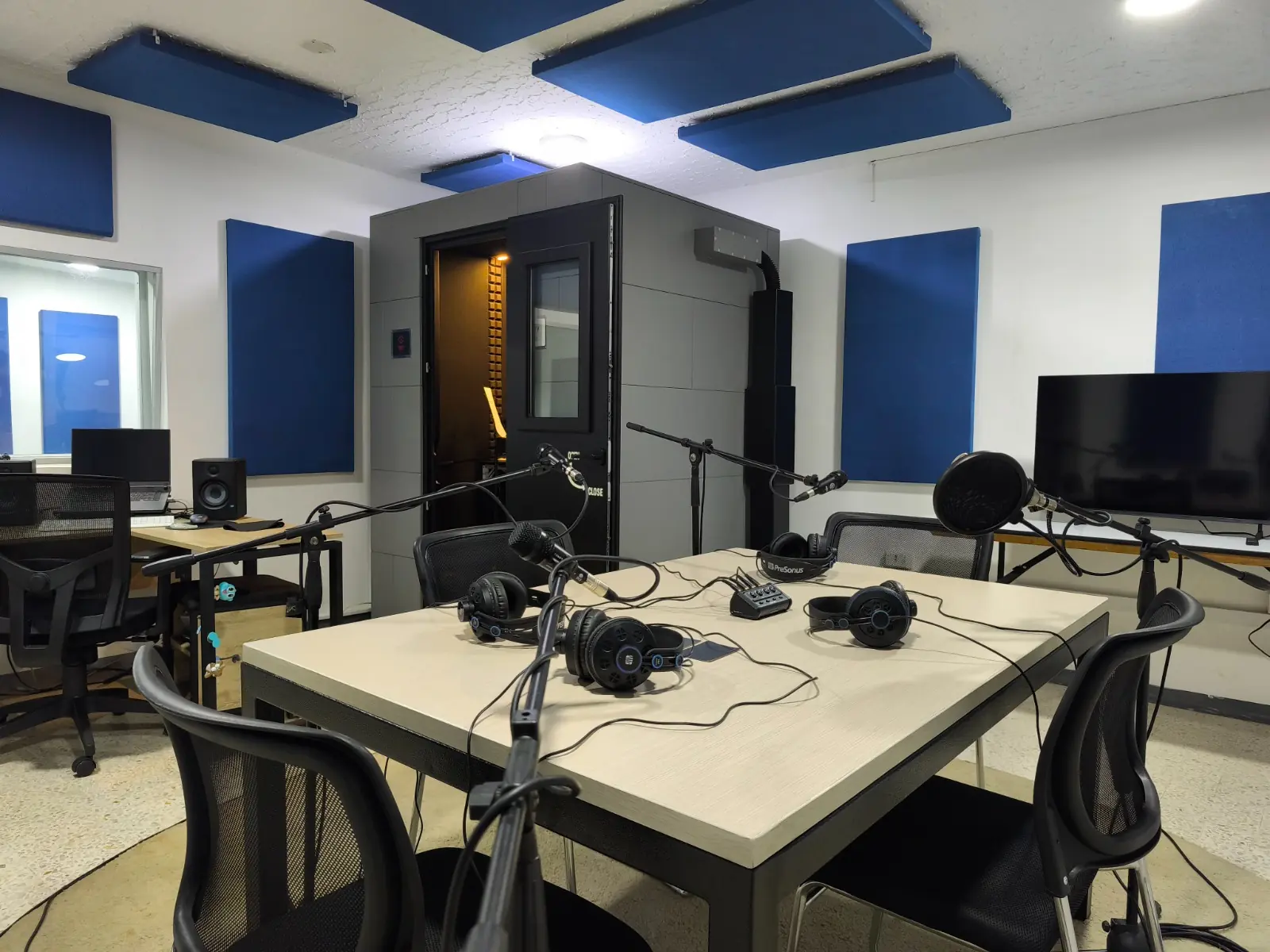 Sala de podcast con mesa, micrófonos y monitores